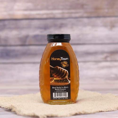 A 16oz glass bottle of HoneyTown Honey, on rustic burlap with a wooden background.