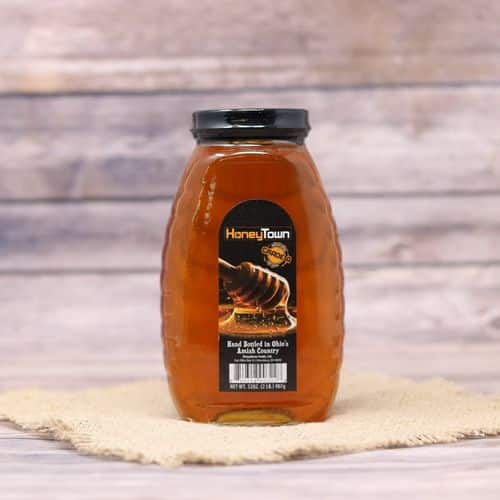 A 2lb glass bottle of HoneyTown Raw Honey, on rustic burlap with a wooden background.