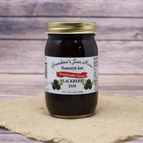 An 18oz glass jar of Grandma's Jam House Blackberry Jam, on rustic burlap with a wooden background.