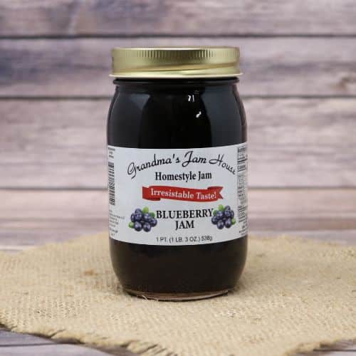 An 18oz glass jar of Grandma's Jam House Blueberry Jam, on rustic burlap with a wooden background.