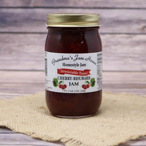 An 18oz glass jar of Grandma's Jam House Cherry Rhubarb Jam, on rustic burlap with a wooden background.