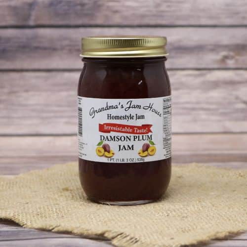 An 18oz glass jar of Grandma's Jam House Damson Plum Jam, on rustic burlap with a wooden background.