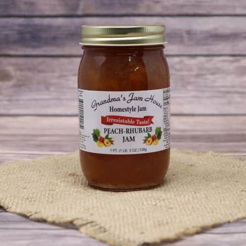 An 18oz glass jar of Grandma's Jam House Peach Rhubarb Jam, on rustic burlap with a wooden background.