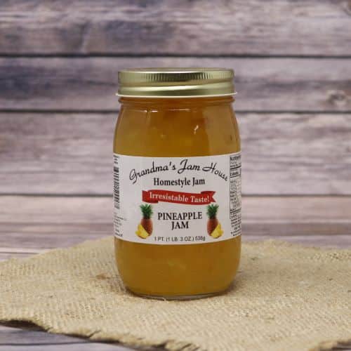 An 18oz glass jar of Grandma's Jam House Pineapple Jam, on rustic burlap with a wooden background.