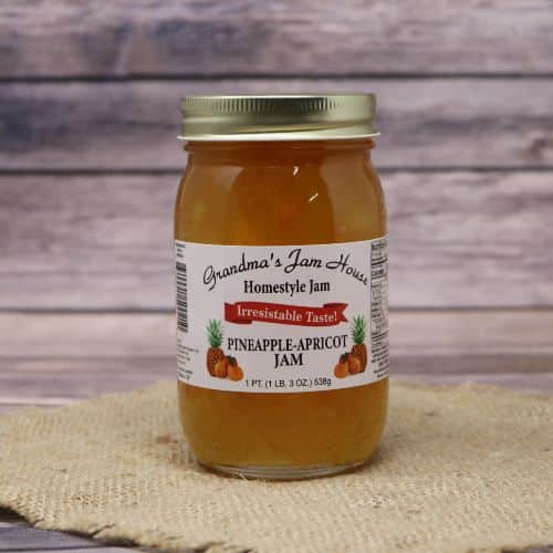 An 18oz glass jar of Grandma's Jam House Pineapple Apricot Jam, on rustic burlap with a wooden background.