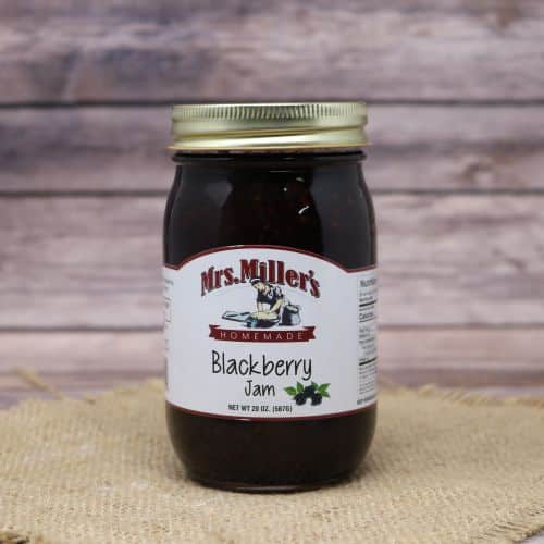 A 20oz glass jar of Mrs. Miller's Blackberry Jam, on rustic burlap with a wooden background.