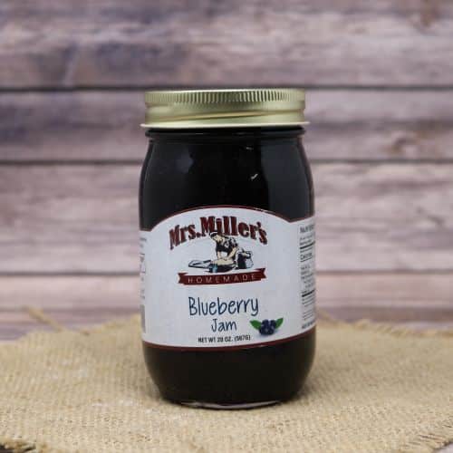 A 20oz glass jar of Mrs. Miller's Blueberry Jam, on rustic burlap with a wooden background.