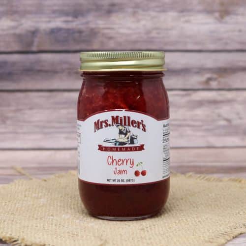 A 20oz glass jar of Mrs. Miller's Cherry Jam, on rustic burlap with a wooden background.