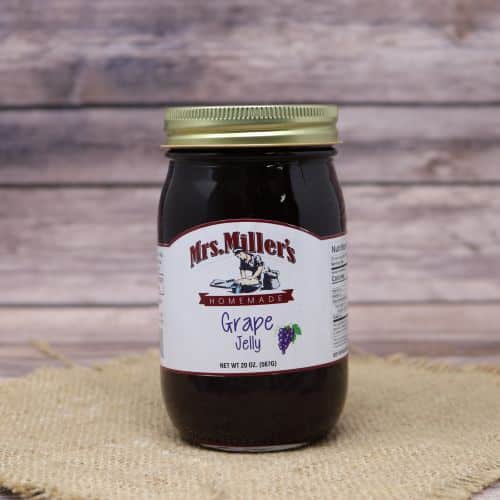 A 20oz glass jar of Mrs. Miller's Grape Jelly, on rustic burlap with a wooden background.