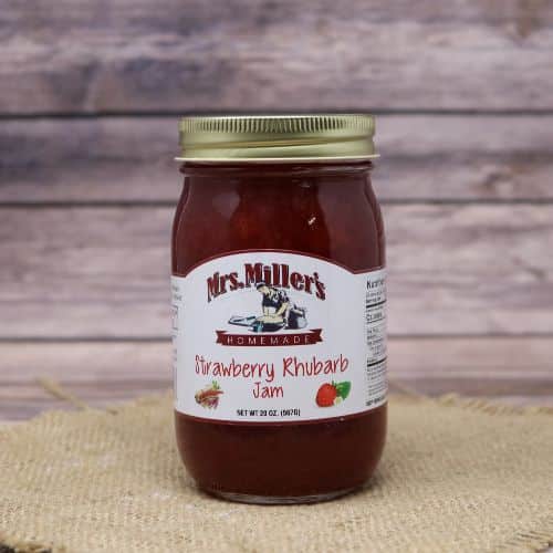 A 20oz glass jar of Mrs. Miller's Strawberry Rhubarb Jam, on rustic burlap with a wooden background.