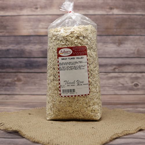 A bag of Hulled Barley Flakes, sealed with a twist tie, on rustic burlap with a wooden background.