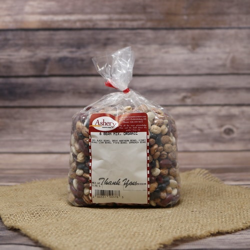 A bag of dried 6 Bean Mix Organic, sealed with a twist tie, on a rustic burlap and wooden background.