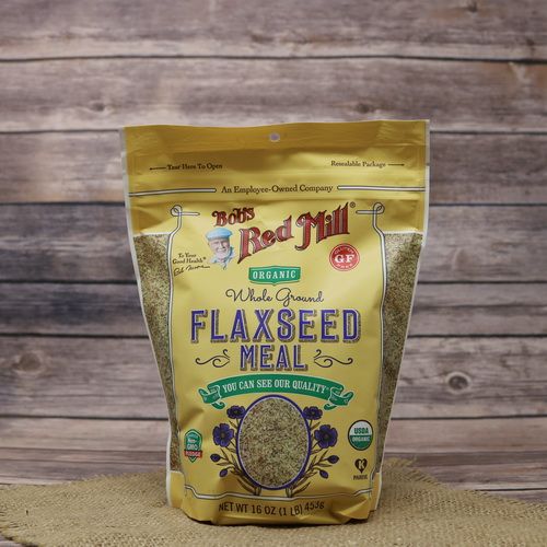 A bag of Bob's Red Mill Organic Brown Flaxseed Meal, on rustic burlap, with a wooden background.