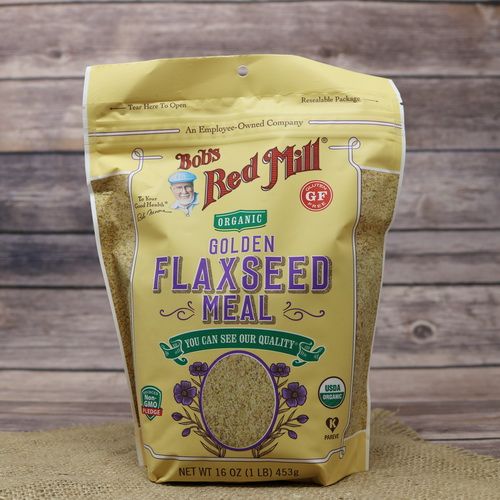 A bag of Bob's Red Mill Organic Golden Flaxseed Meal, on rustic burlap, with a wooden background.