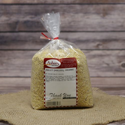 A bag of Hulled Millet Organic, sealed with a twist tie, on rustic burlap with a wooden background.