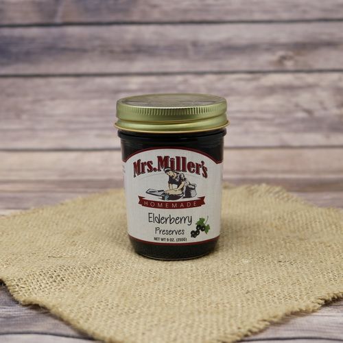 A 9oz glass jar of Mrs. Miller's Homemade Elderberry Preserves, on rustic burlap with a wooden background.