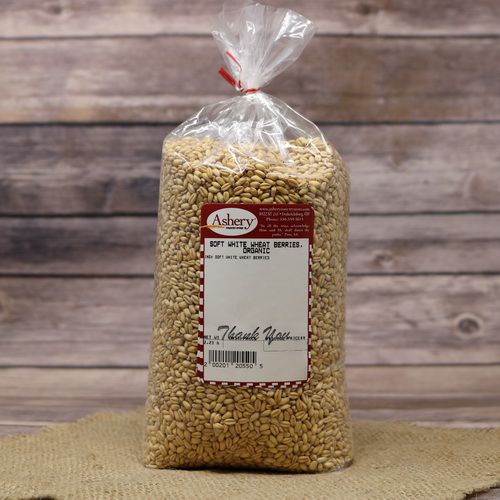 A bag of Soft White Wheat Berries Organic, sealed with a twist tie, on rustic burlap with a wooden background.