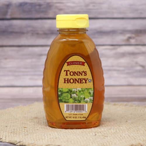 A 16oz bottle of Tonn's Clover Honey, on rustic burlap with a wooden background.