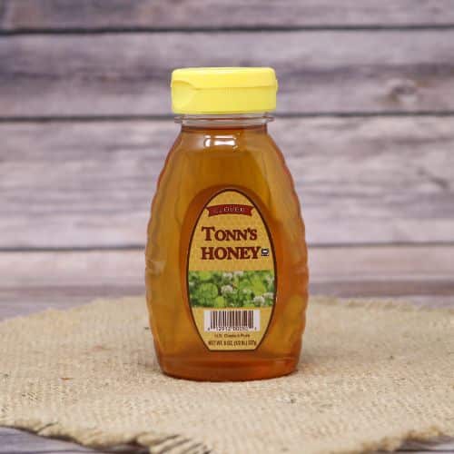 An 8oz bottle of Tonn's Clover Honey, on rustic burlap with a wooden background.