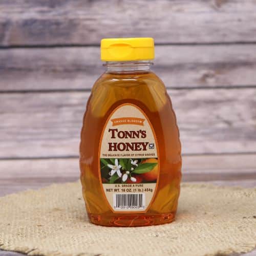 A bottle of Orange Blossom Honey, on rustic burlap with a wooden background.