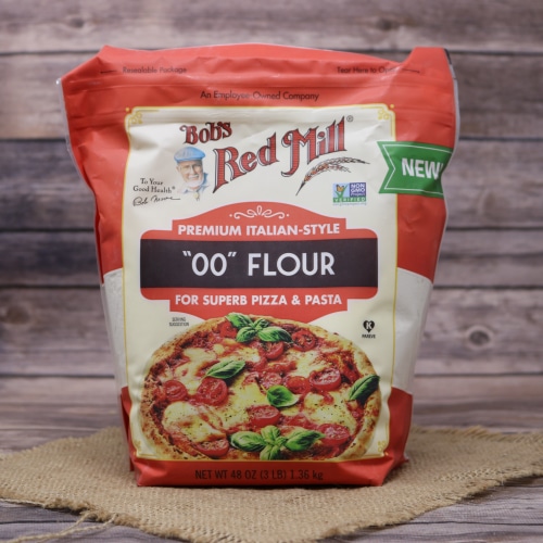 Package of Bob's Red Mill '00' Flour for pizza and pasta, with a vibrant red design, on a burlap and wood surface.