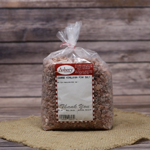 Bag of Ashery Coarse Himalayan Pink Salt, with a red and white label, on a burlap cloth and wooden surface.