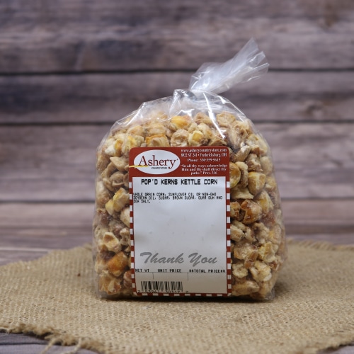 Clear bag of Ashery's Pop'd Kerns Kettle Corn on a natural burlap cloth with a wood texture in the background.