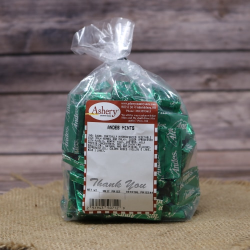A bag of Andes Mints candy, individually wrapped in green foil, gathered on a straw mat with a wooden texture backdrop.
