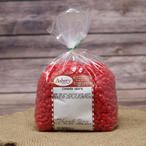 Bag of Ashery's Cinnamon Hearts Candy in vibrant red, sealed with a twist tie, on a rustic burlap and wooden background.