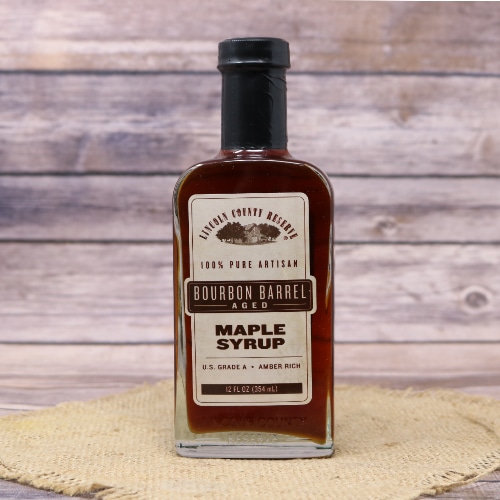 A glass bottle of Bourbon Aged Maple Syrup on rustic burlap and a wooden background.