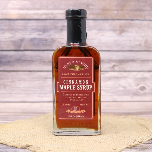 A glass bottle of Cinnamon Maple Syrup on rustic burlap and a wooden background.