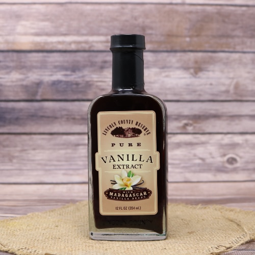 A glass bottle of Vanilla Extract Pure on rustic burlap and a wooden background.