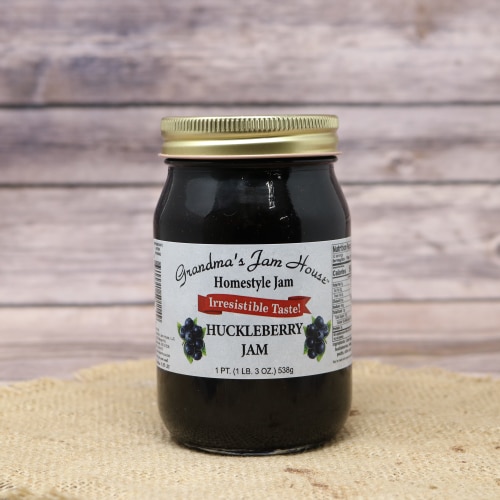 A pint jar of Huckleberry Jam made by Grandma's Jam House on rustic burlap with a wooden background.