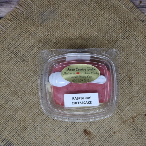 A small clear container of Raspberry Cheesecake Fudge on with a small spoon rustic burlap with a wooden background.